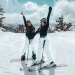 Two women posing on a snowy slope, enjoying a bright winter day of skiing and snowboarding.