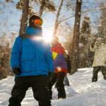 Group of snowboarders enjoying a sunny winter day in the snowy woods, wearing colorful jackets.