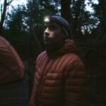 A man with a headlamp in a forest at night, near a tent in Torres del Paine.